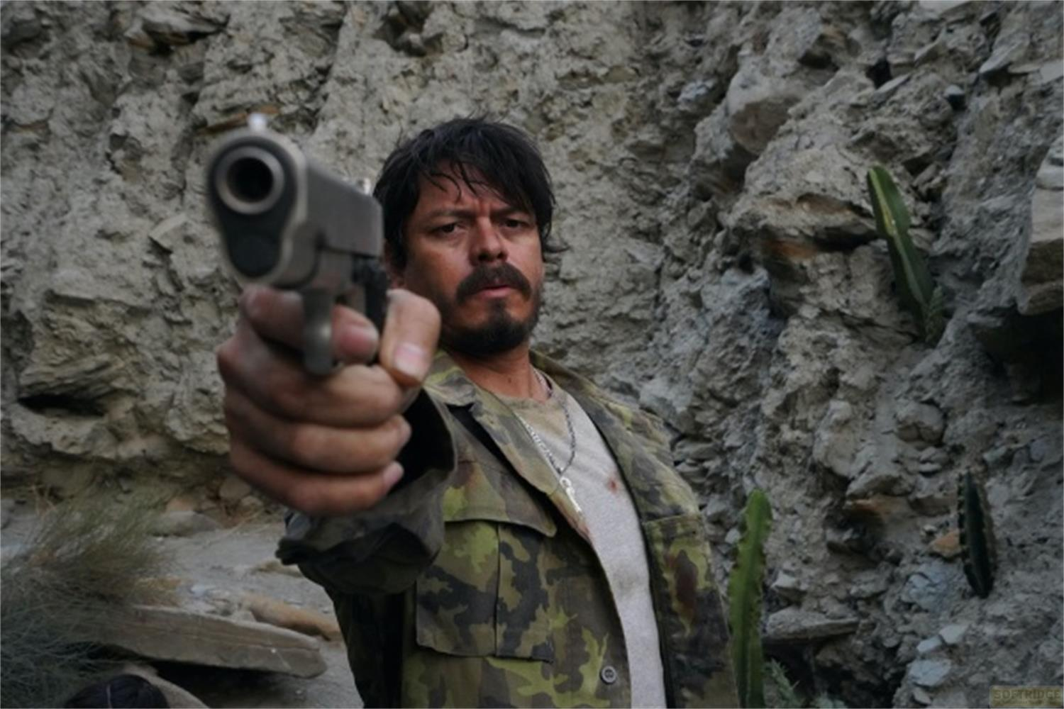 Uomo con pistola davanti a muro roccioso e cactus