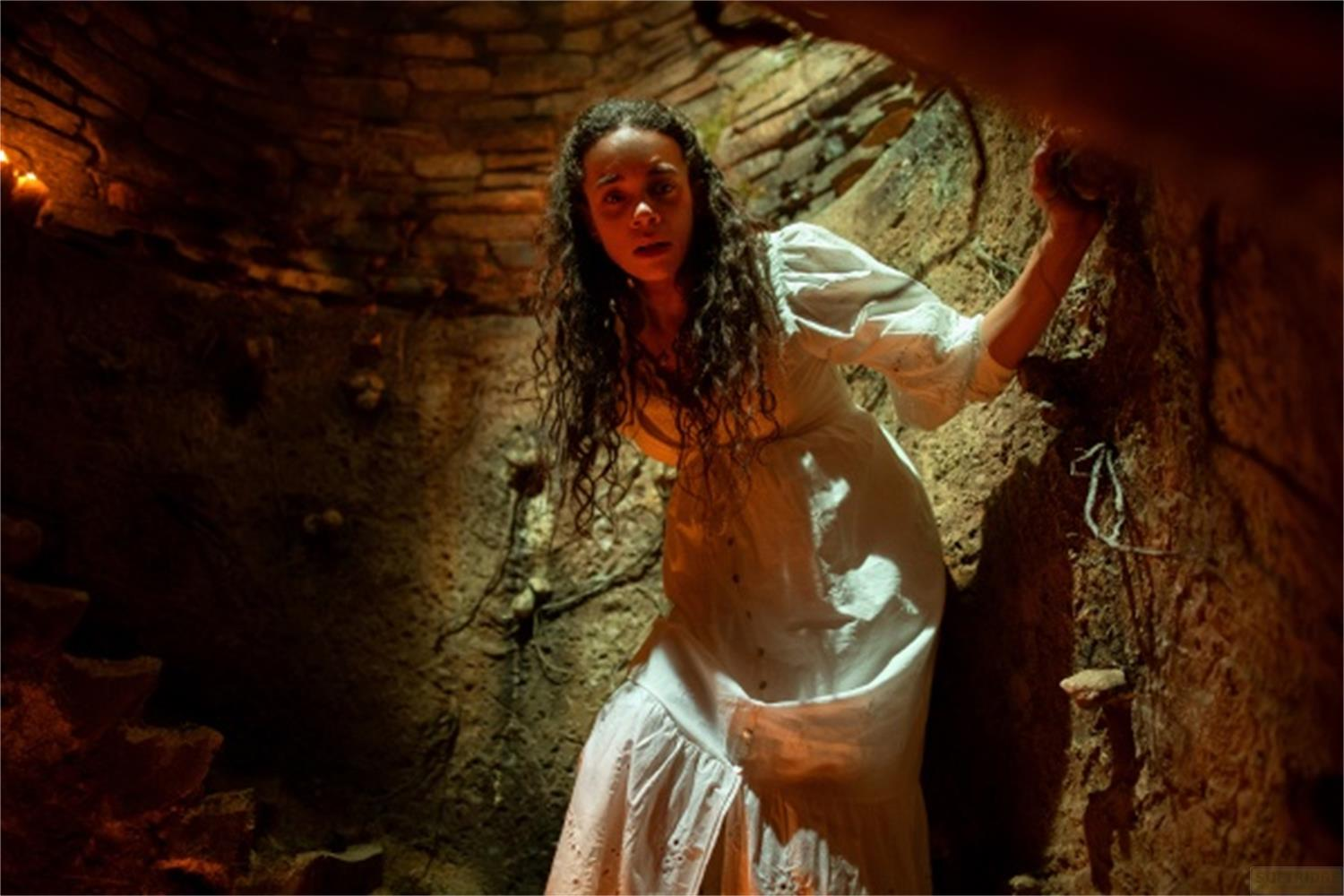 Una donna in un vestito bianco si trova in una grotta, spaventata.