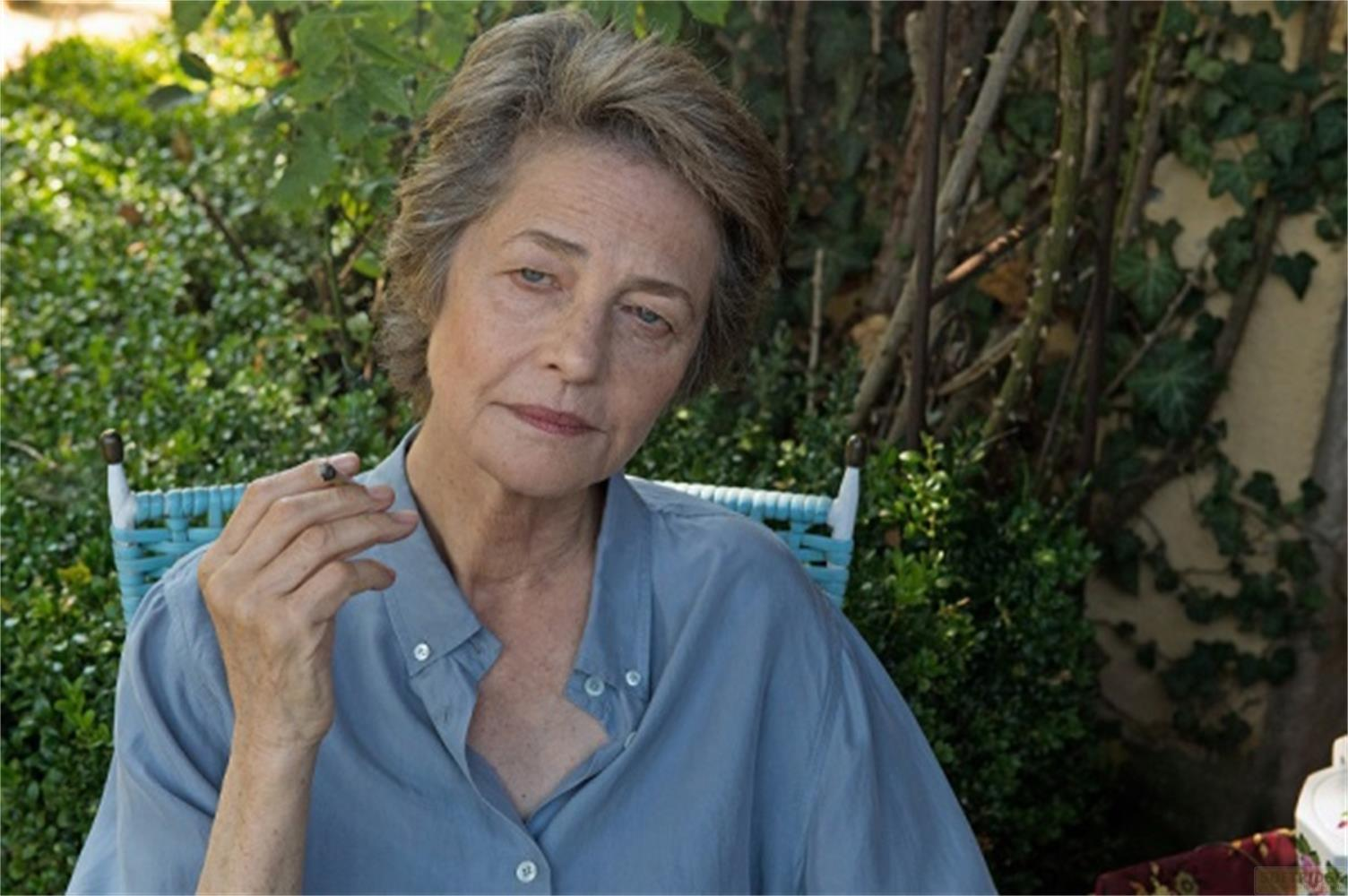 Donna anziana con capelli grigi fuma una sigaretta all'aperto, camicia blu.
