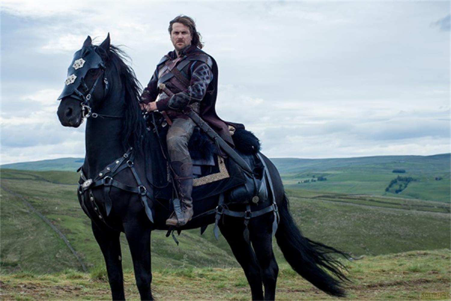 Un homme aux cheveux sombres monte un cheval noir avec armure.