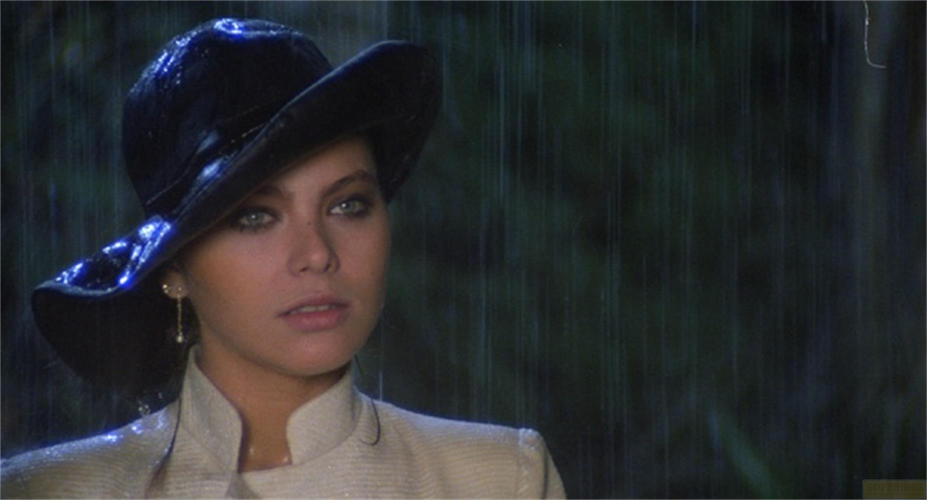 Donna con cappello nero e cappotto beige sotto la pioggia.