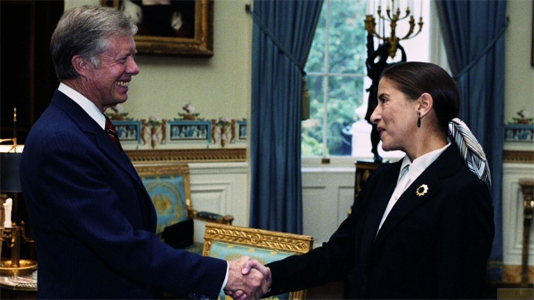 Jimmy Carter e Ruth Bader Ginsburg si stringono la mano in un ufficio.
