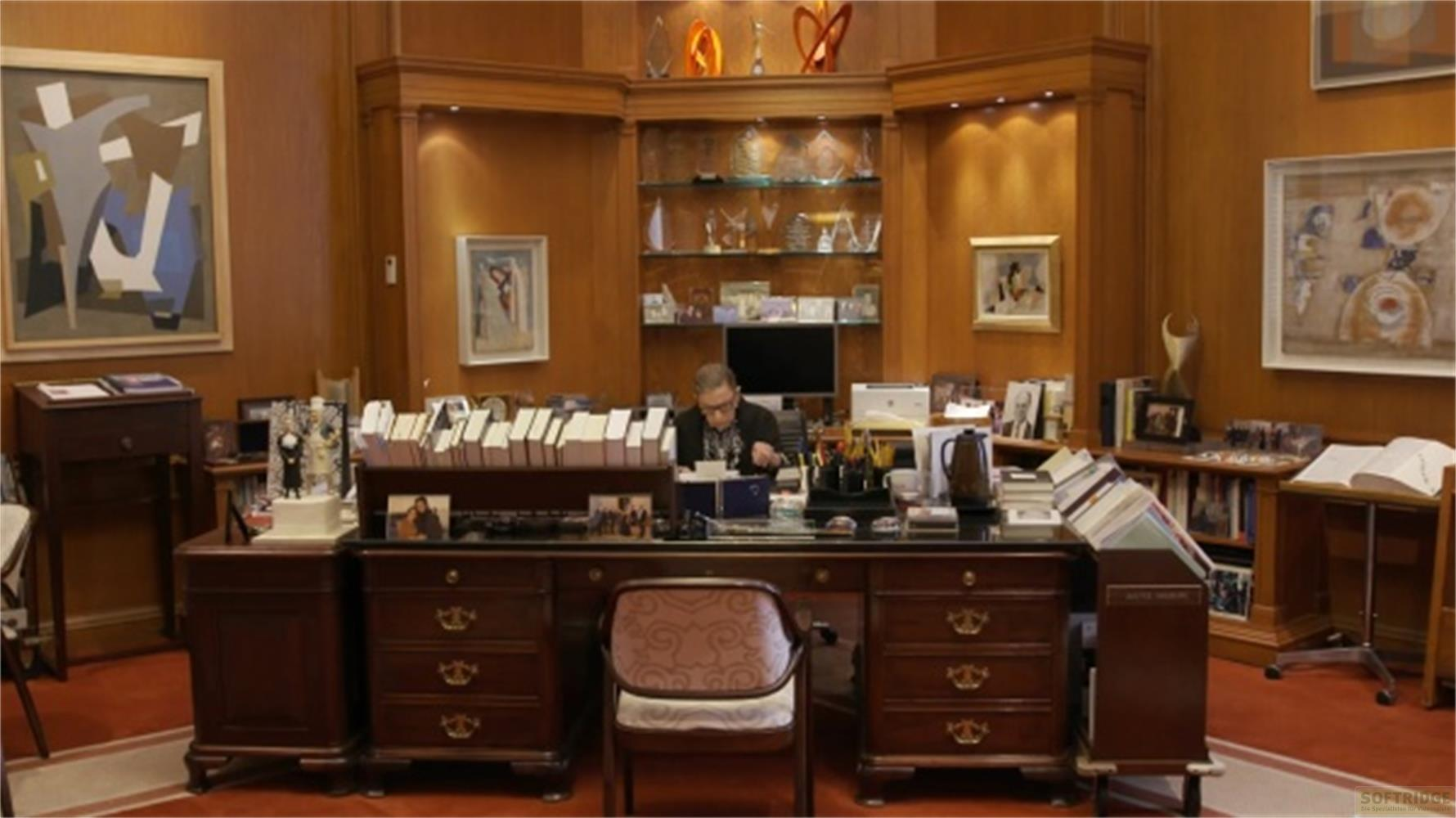 Un uomo siede a una scrivania in un ufficio con pannelli in legno pieno di libri e opere d'arte.
