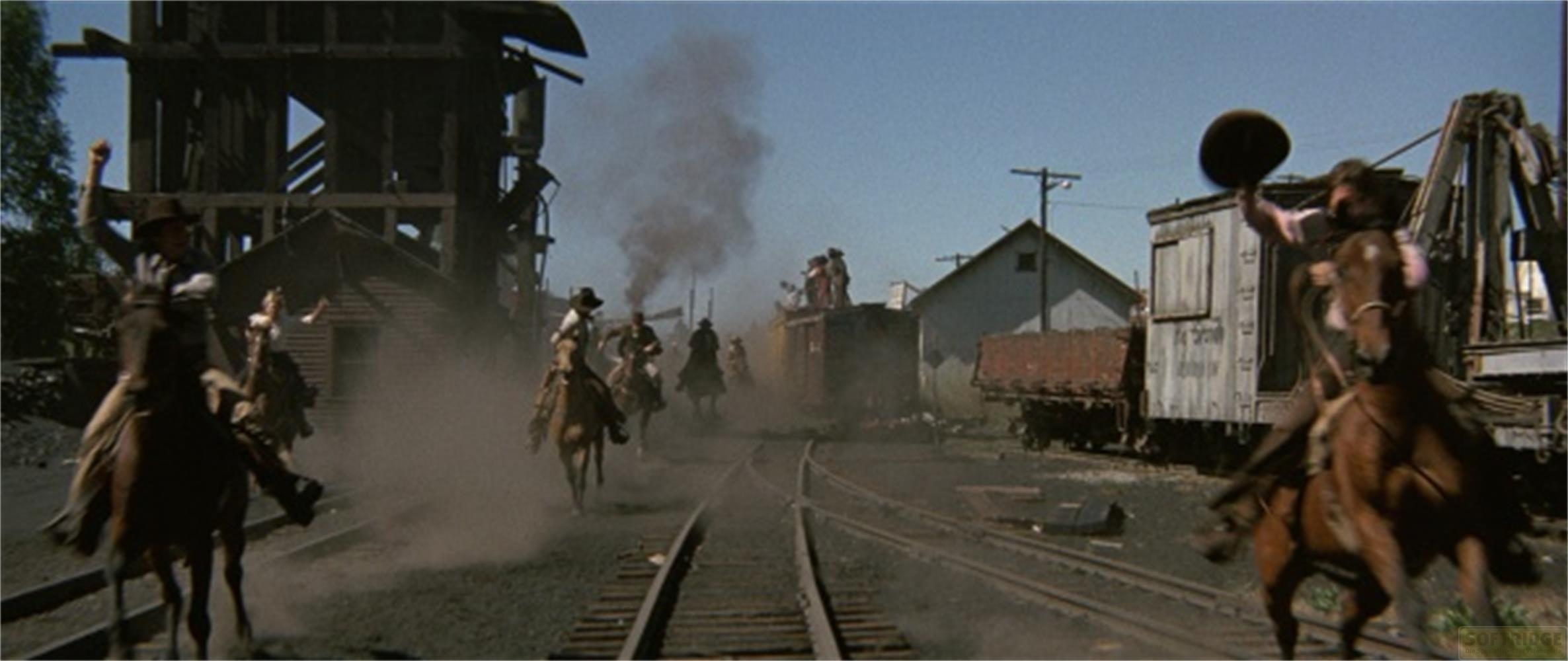 Cowboys reiten auf Pferden in einer staubigen Stadt mit Zügen und Gebäuden.