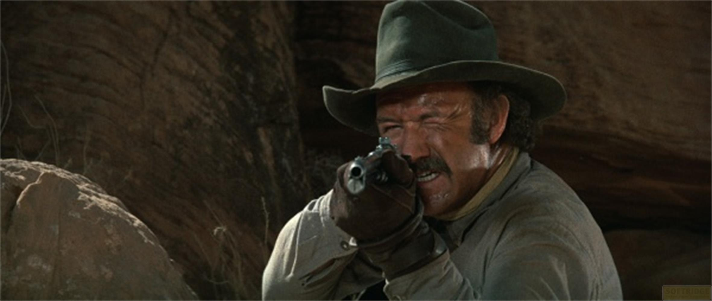 Ein Mann im Westernhut zielt mit einer Pistole, im Hintergrund felsige Landschaft.