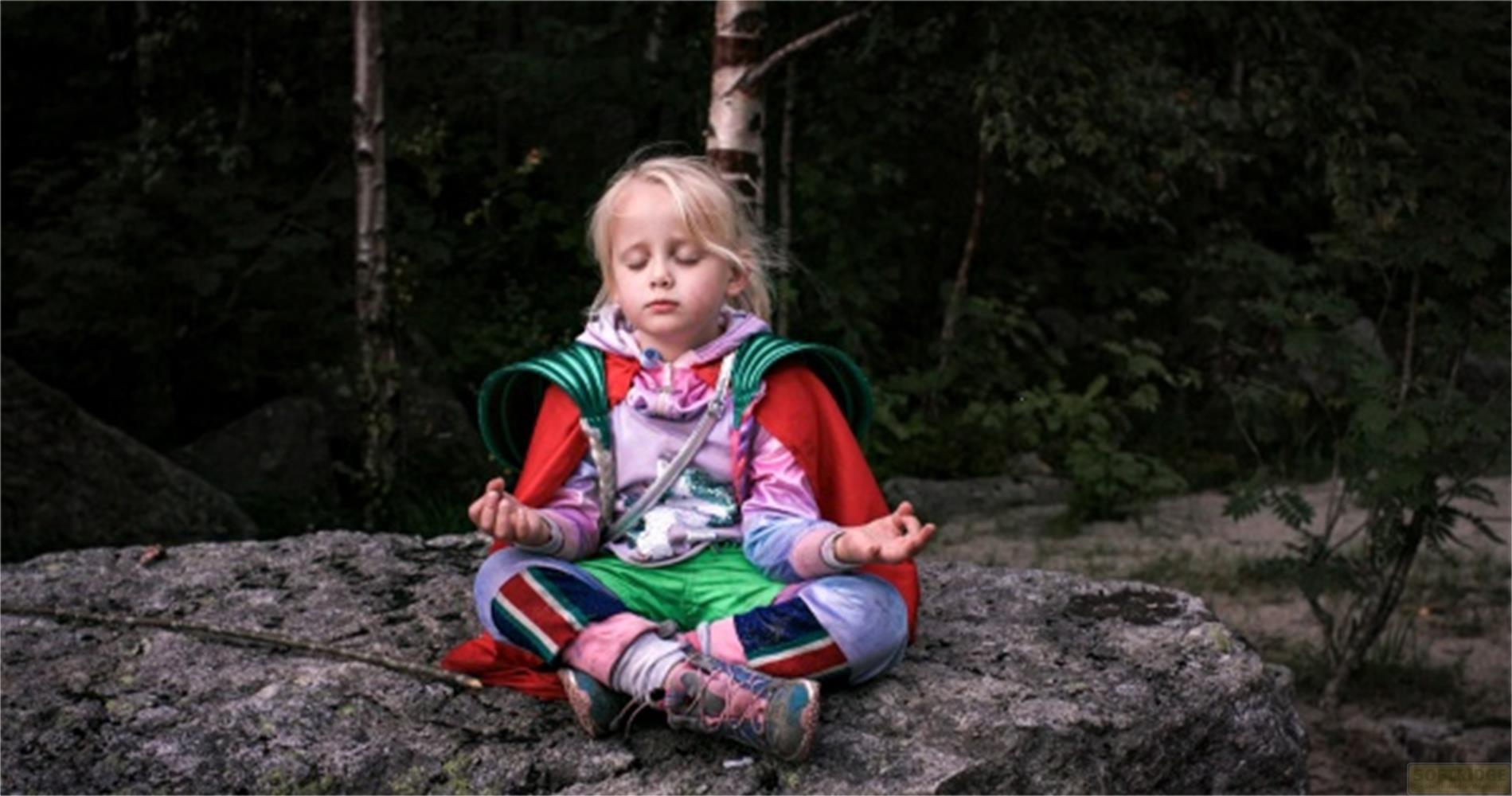 Una bambina medita su una roccia in una foresta.