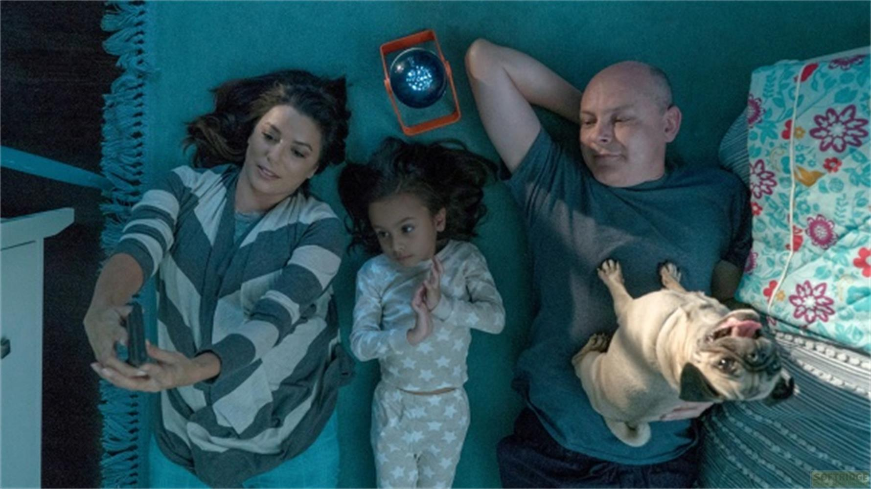 Una famiglia con un carlino giace su un tappeto sotto un proiettore di stelle.