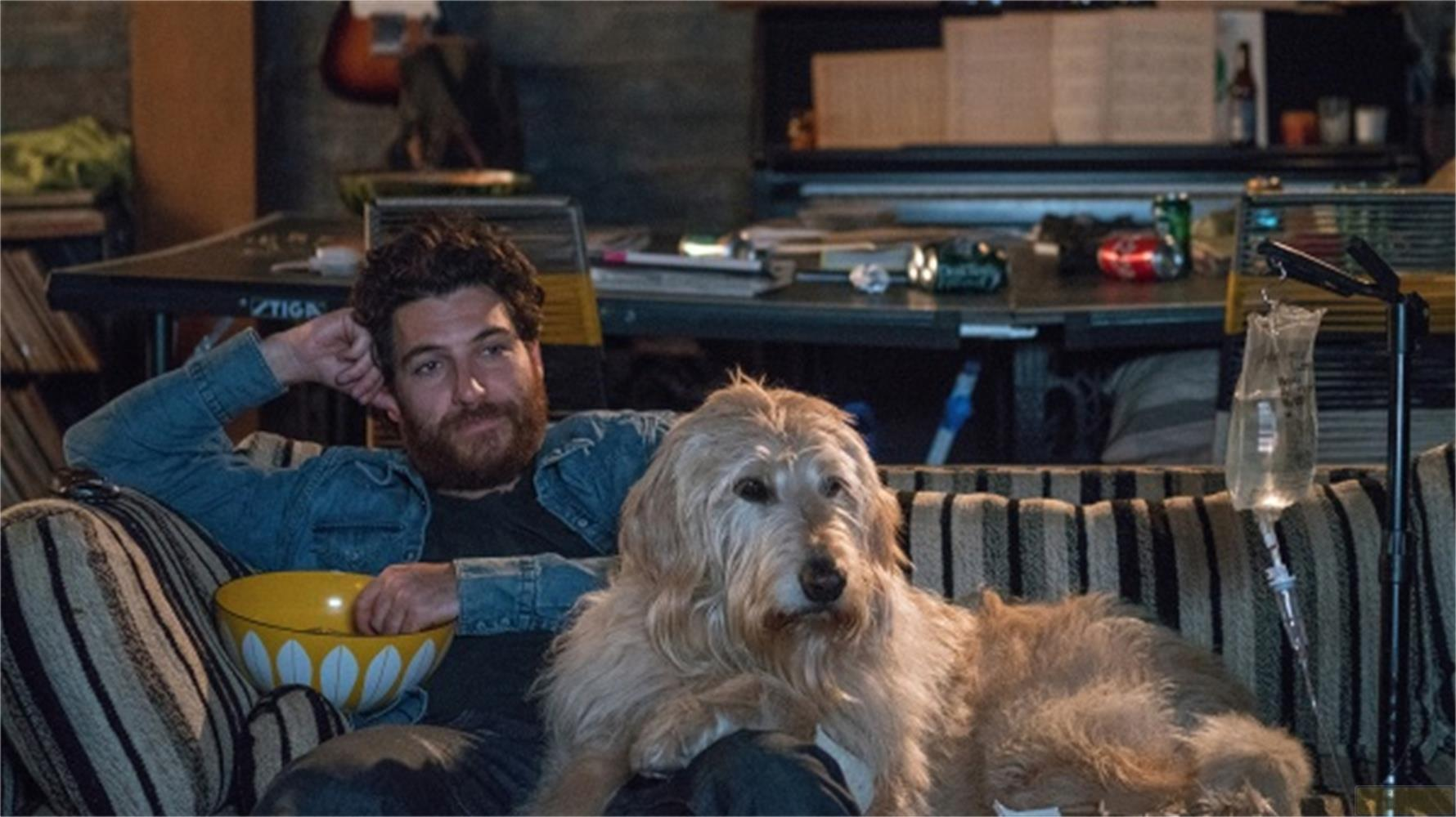 Un uomo con la barba e un cane seduti su un divano, con una ciotola di popcorn nelle vicinanze.