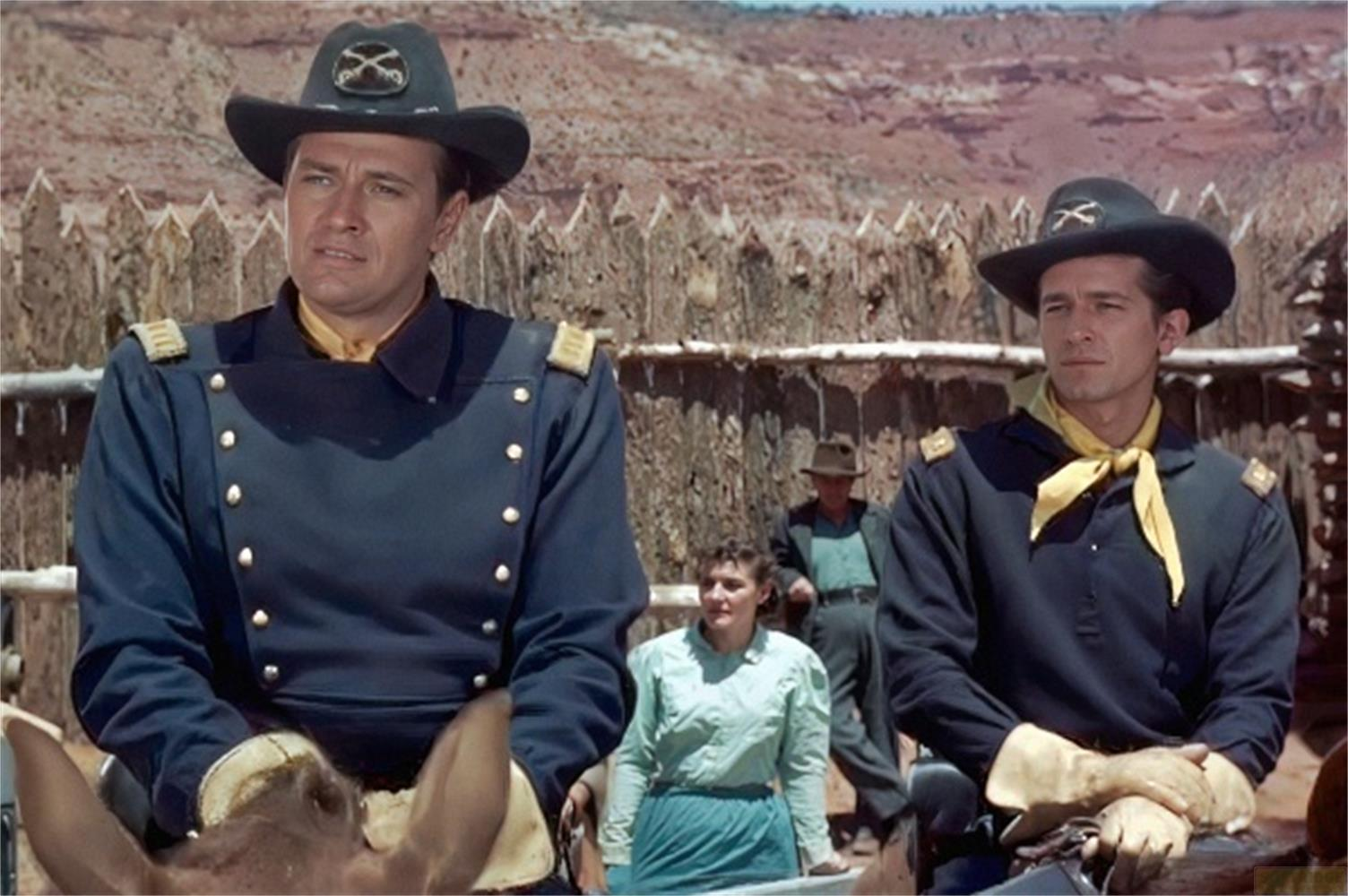 Due cavalieri in uniforme davanti a una palizzata. Paesaggio desertico sullo sfondo.