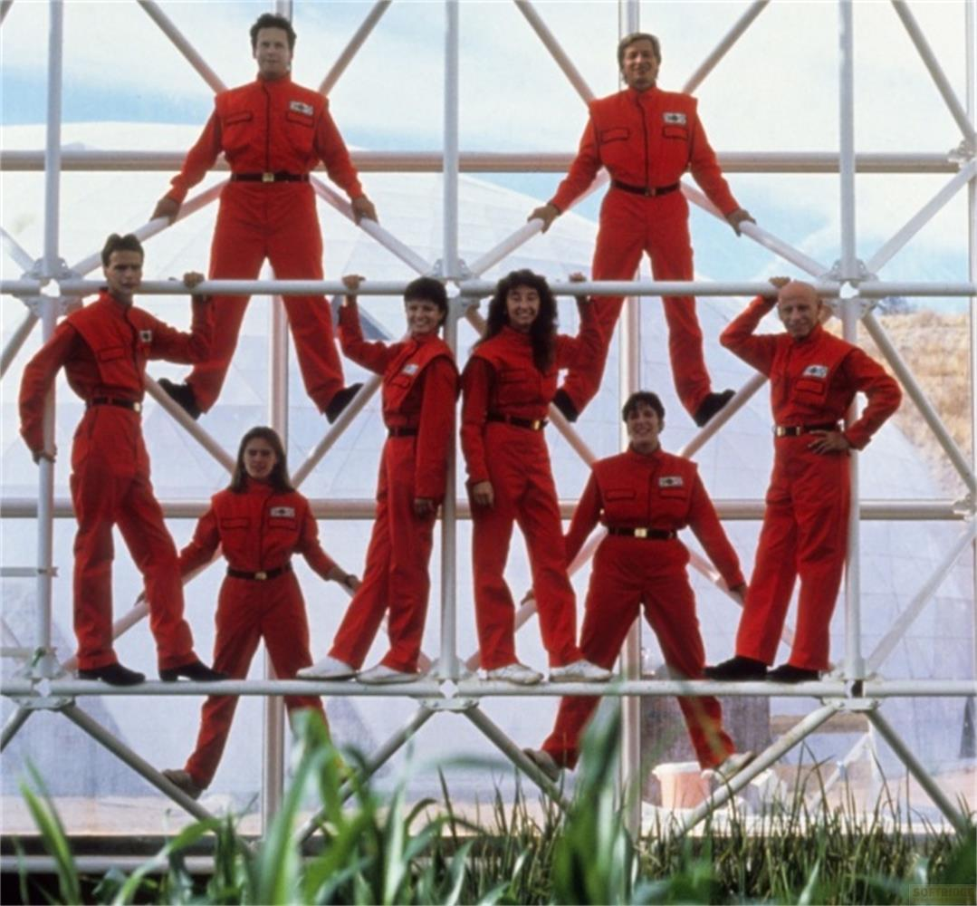 Nove persone in tute rosse stanno su una struttura metallica.
