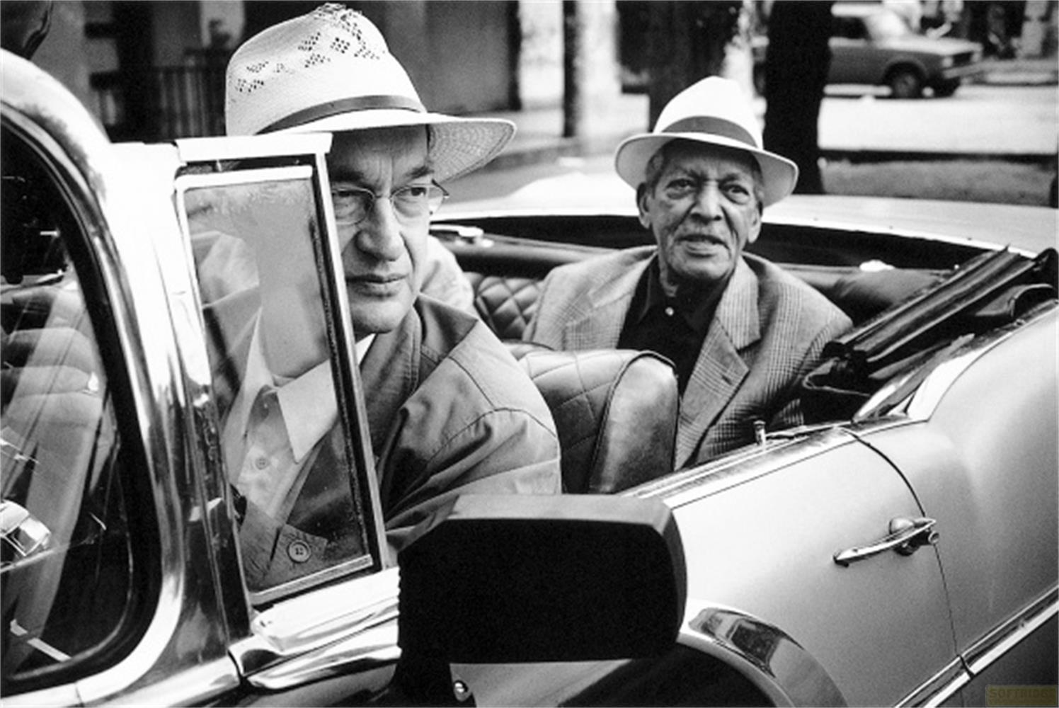 Due uomini con cappelli siedono in una decappottabile. Uno guarda a sinistra.