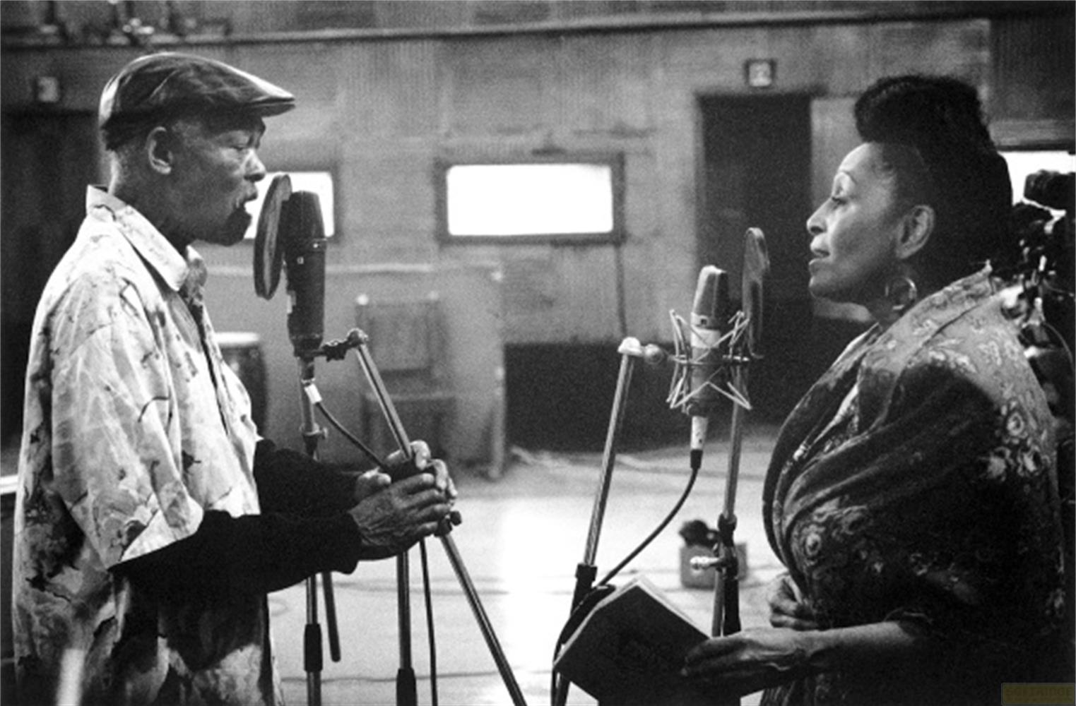 Un uomo e una donna cantano nei microfoni in uno studio.