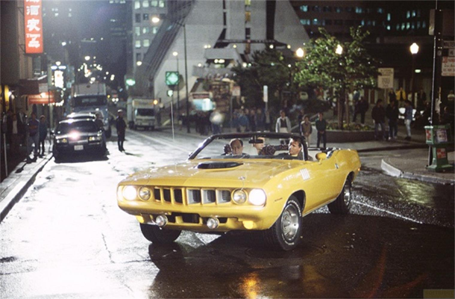 Una convertibile vintage gialla con due uomini percorre una strada bagnata di notte.