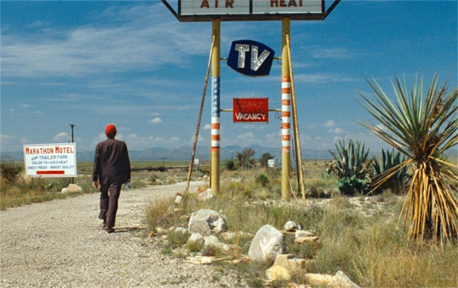 Un uomo cammina su una strada sterrata verso un cartello del Marathon Motel.