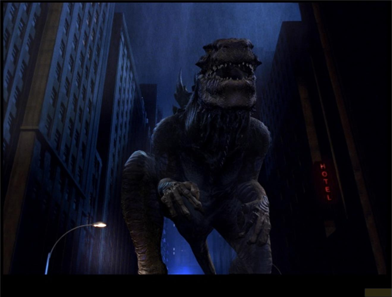 Godzilla se tient dans une rue de ville pluvieuse entre de hauts immeubles.