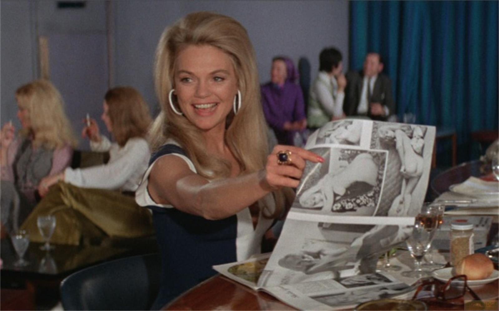 Une femme blonde montre une revue avec des photos.