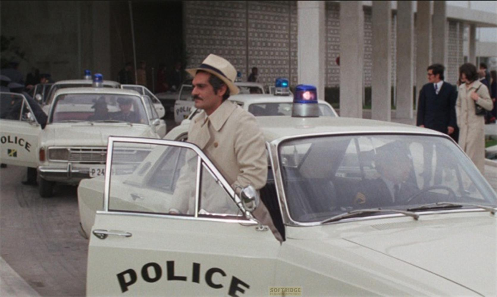 Un homme en manteau beige sort d'une voiture de police.