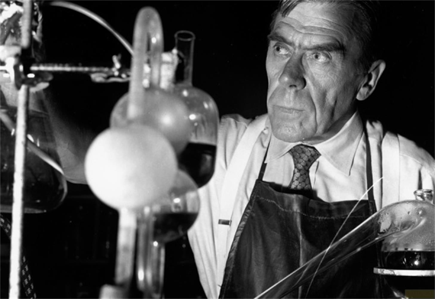 Un homme en blouse et tablier de laboratoire expérimente avec de la verrerie.