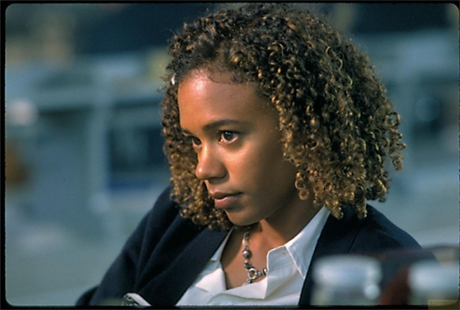 Une jeune femme aux cheveux bouclés porte un chemisier blanc et un blazer sombre.