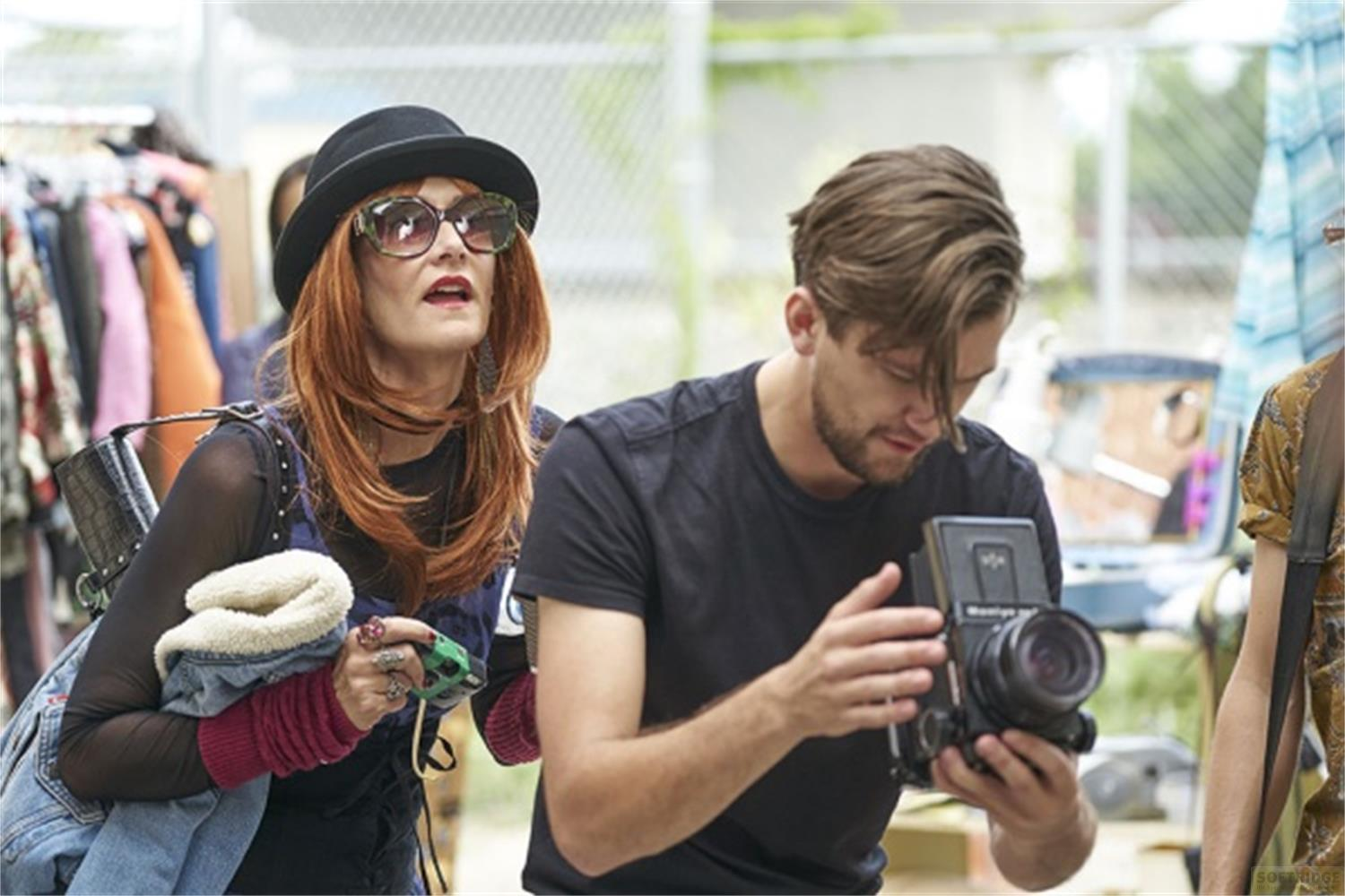 Una donna con cappello e occhiali da sole tiene una macchina fotografica, un uomo tiene una macchina fotografica.