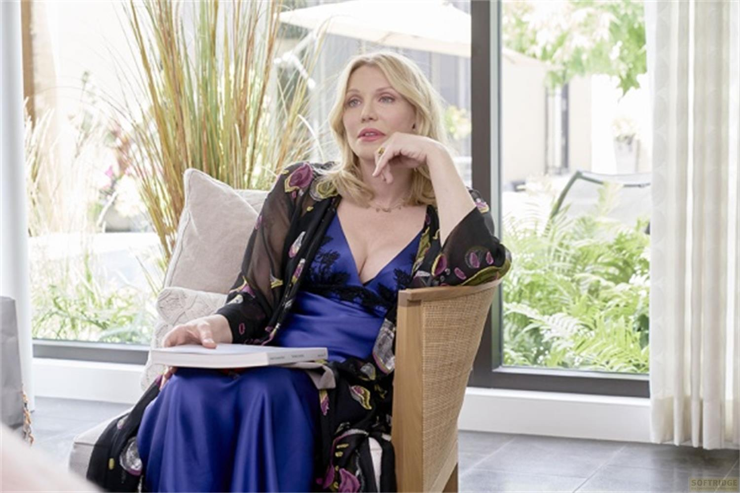 Una donna seduta su una poltrona con un libro, indossa un abito blu e un kimono fantasia.