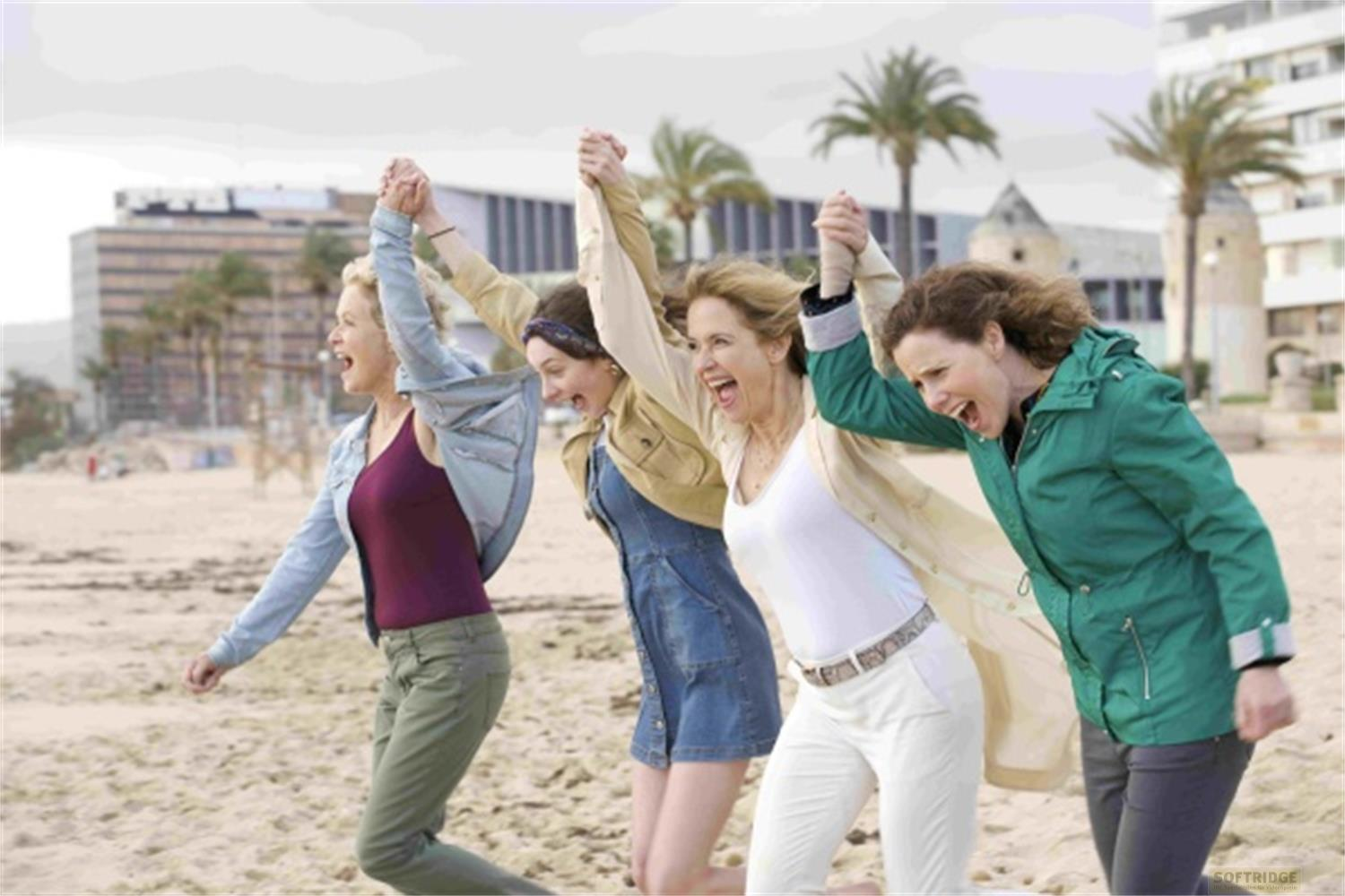 Quattro donne corrono gioiosamente sulla spiaggia.