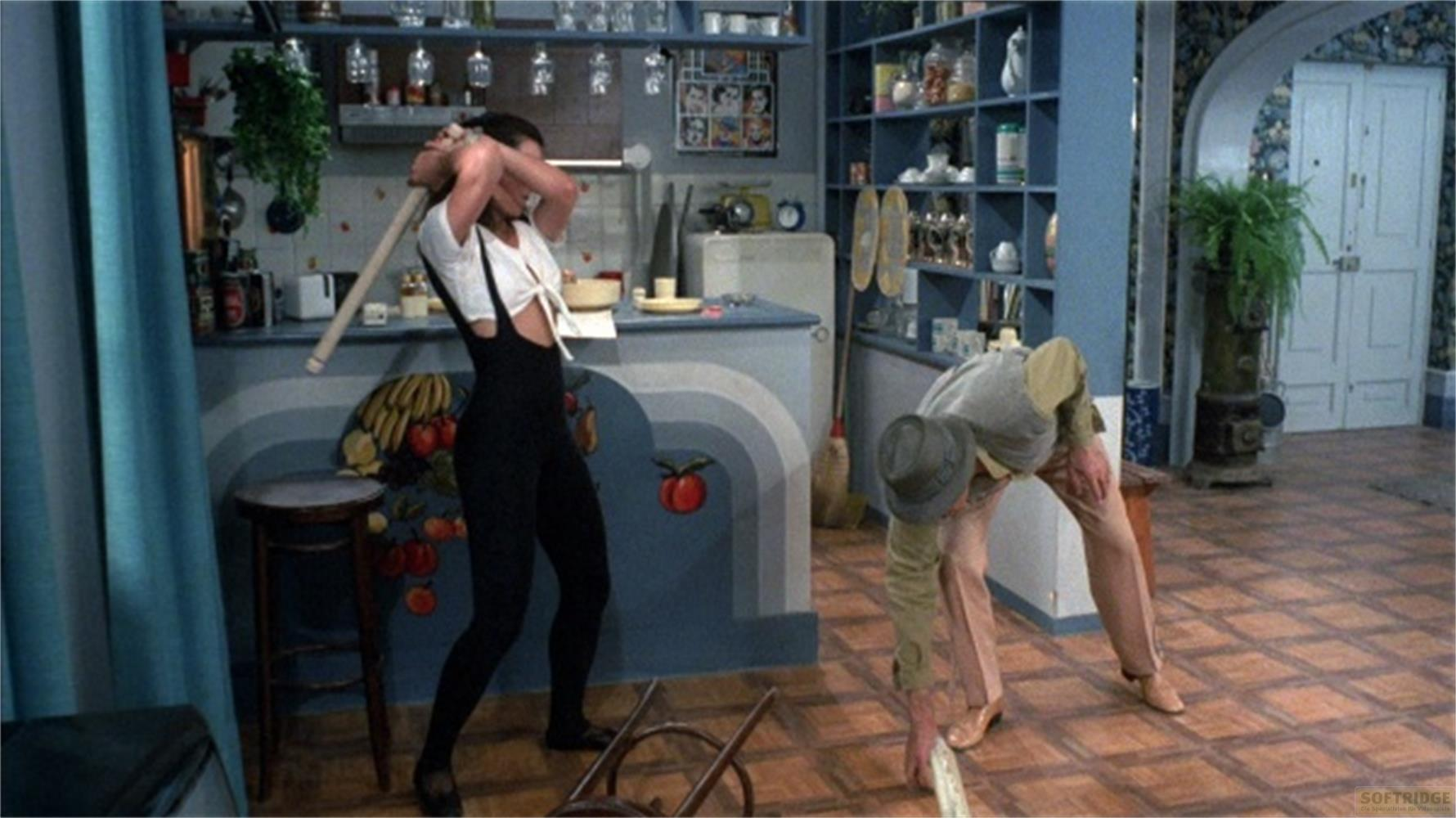 Una donna brandisce un'ascia; un uomo si china in una cucina.