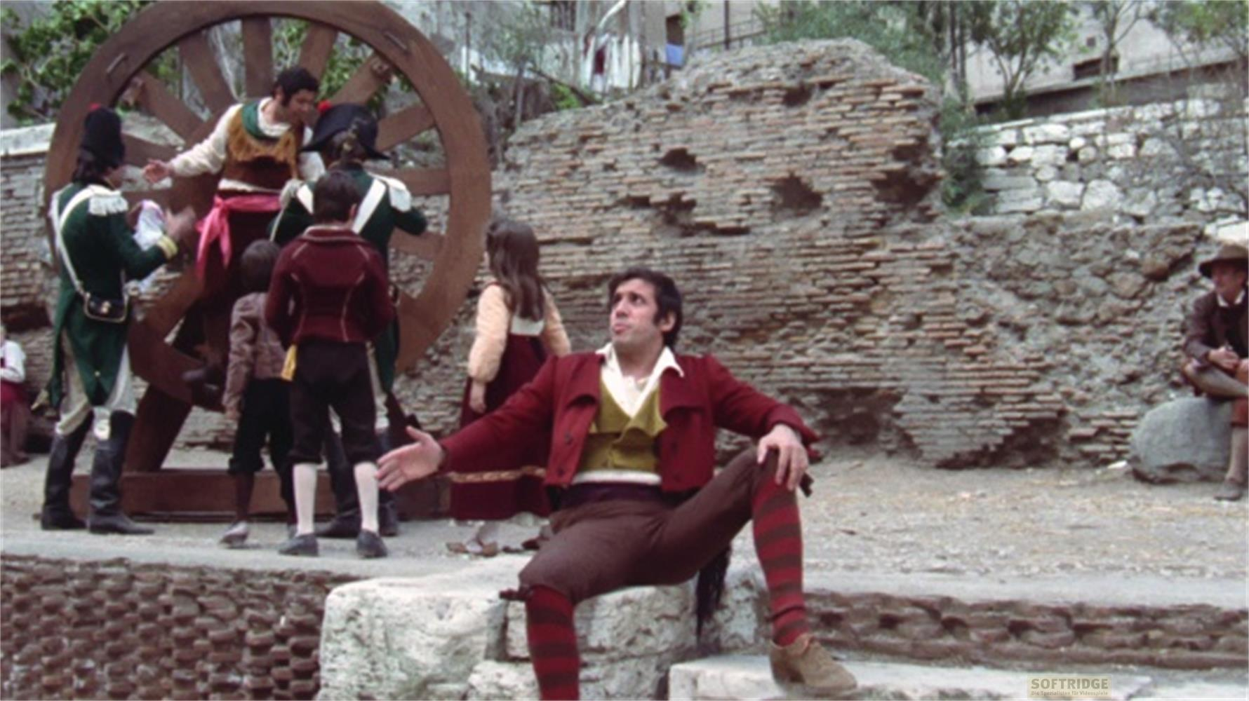 Un gruppo di persone in costume storico con una grande ruota di legno sullo sfondo.