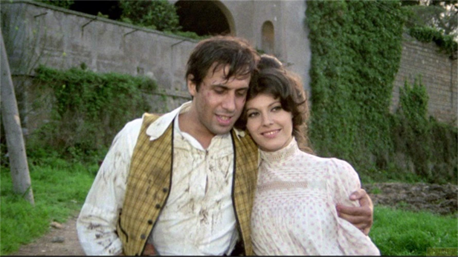 Un uomo e una donna si abbracciano davanti a un muro coperto d'edera.
