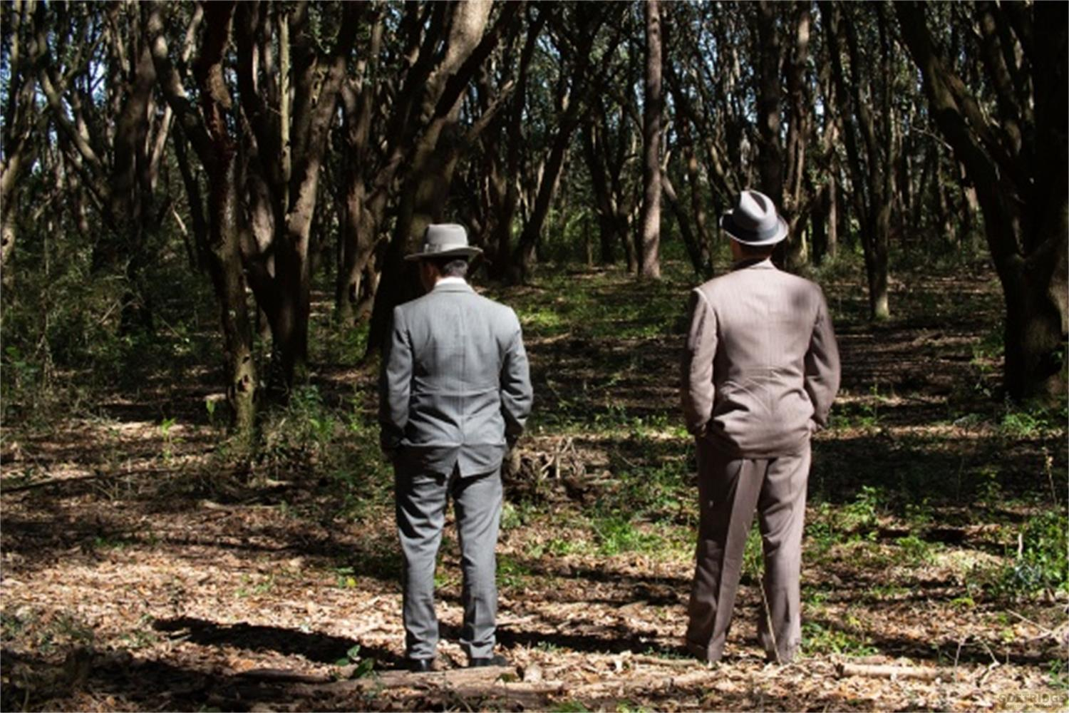Due uomini in abito e cappello stanno in una foresta scura.