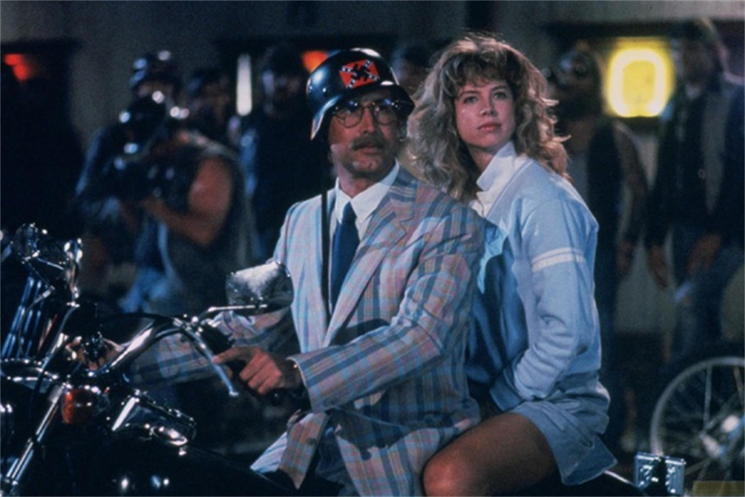 Uomo in casco e completo a quadri su moto, donna dietro.