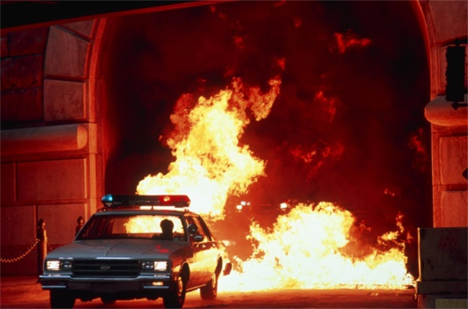 Voiture de police devant un tunnel avec de grandes flammes et de la fumée.