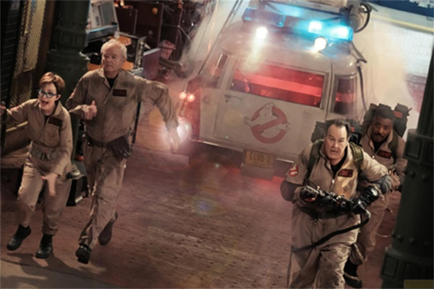 Quattro Ghostbusters in uniforme corrono davanti all'auto Ecto-1, che emette luce blu.