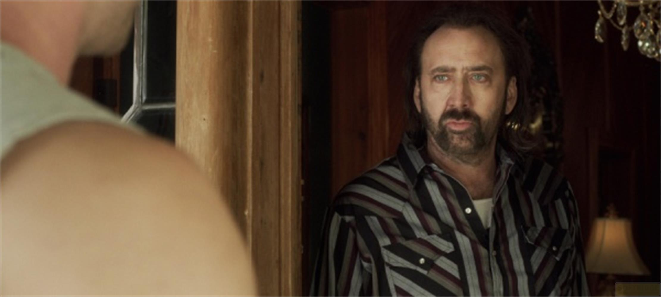 Un uomo con barba e camicia a righe guarda a sinistra.
