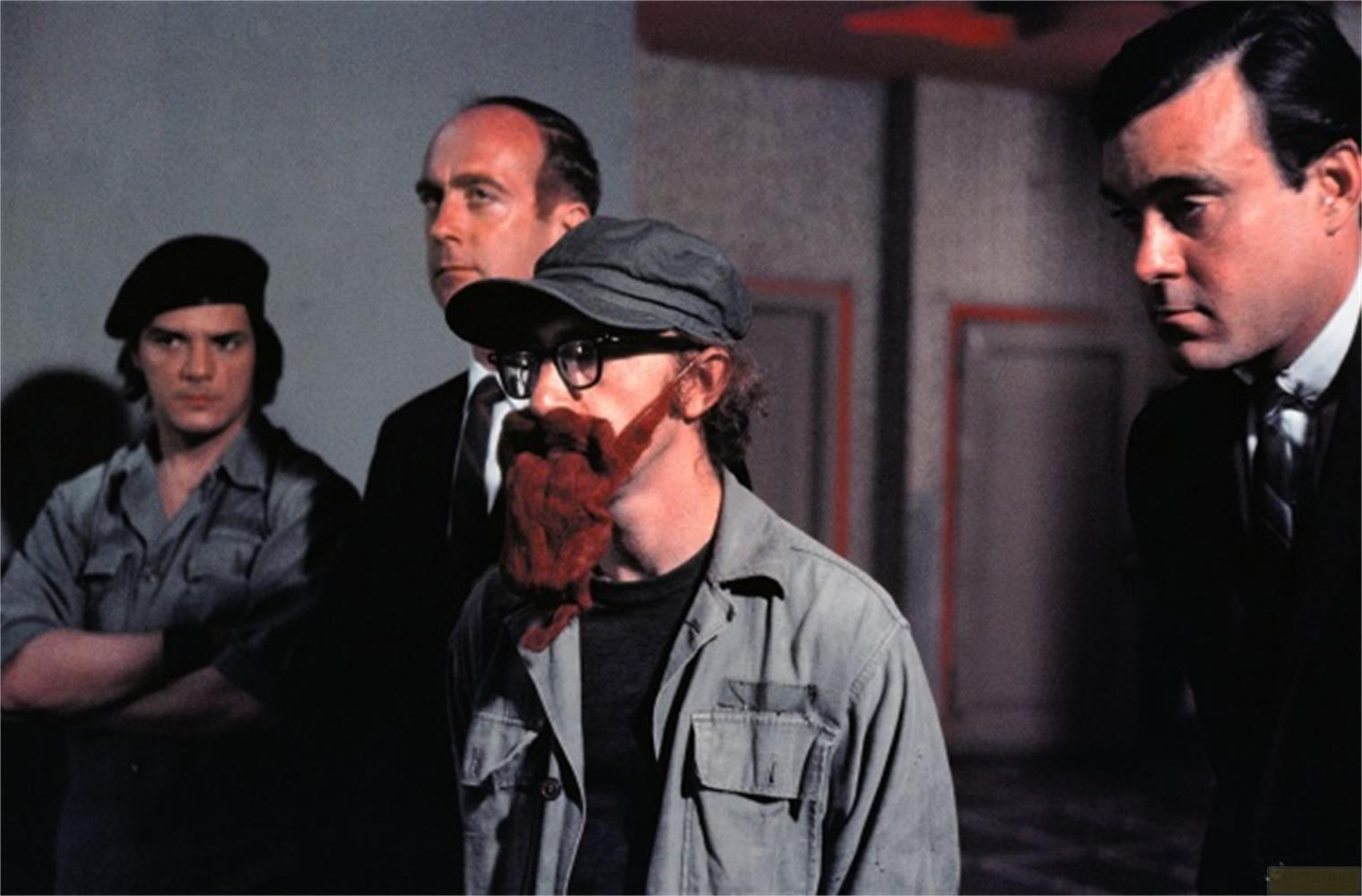 Quattro uomini in piedi in primo piano. Uno porta una barba rossa.