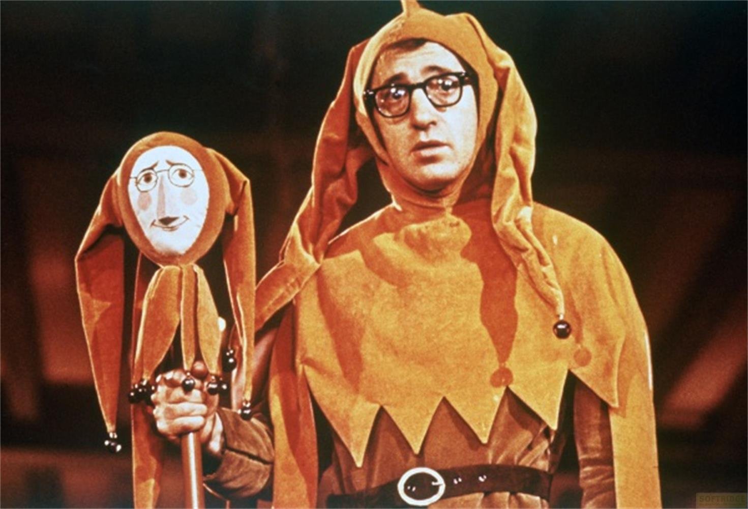Uomo in costume da giullare arancione tiene un burattino simile.
