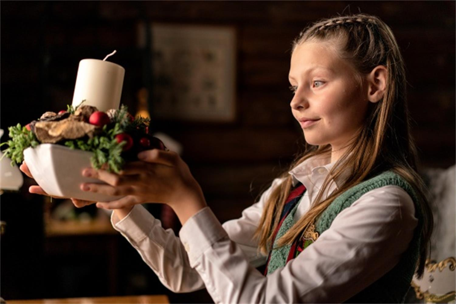 Mädchen hält einen Kerzen-Adventskranz mit Beeren und Grünzeug.