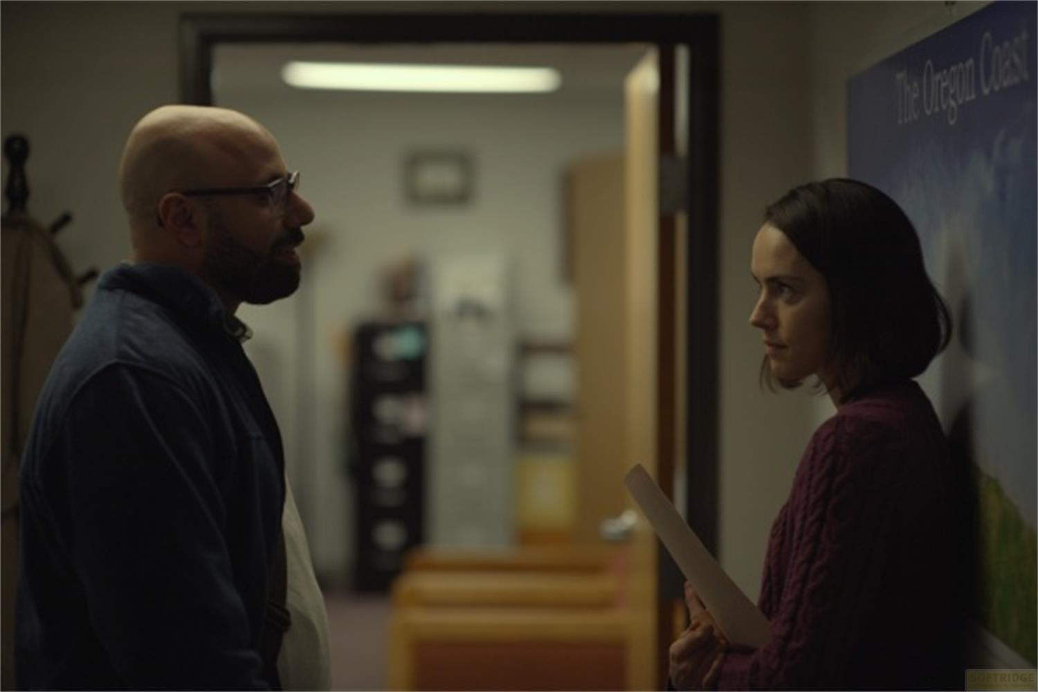 Un uomo calvo con occhiali parla con una donna in maglione.