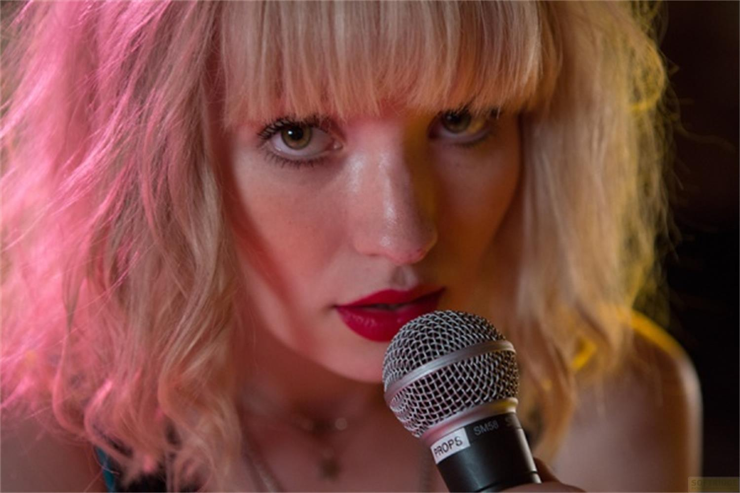 Une femme aux cheveux blonds et lèvres rouges tient un microphone.
