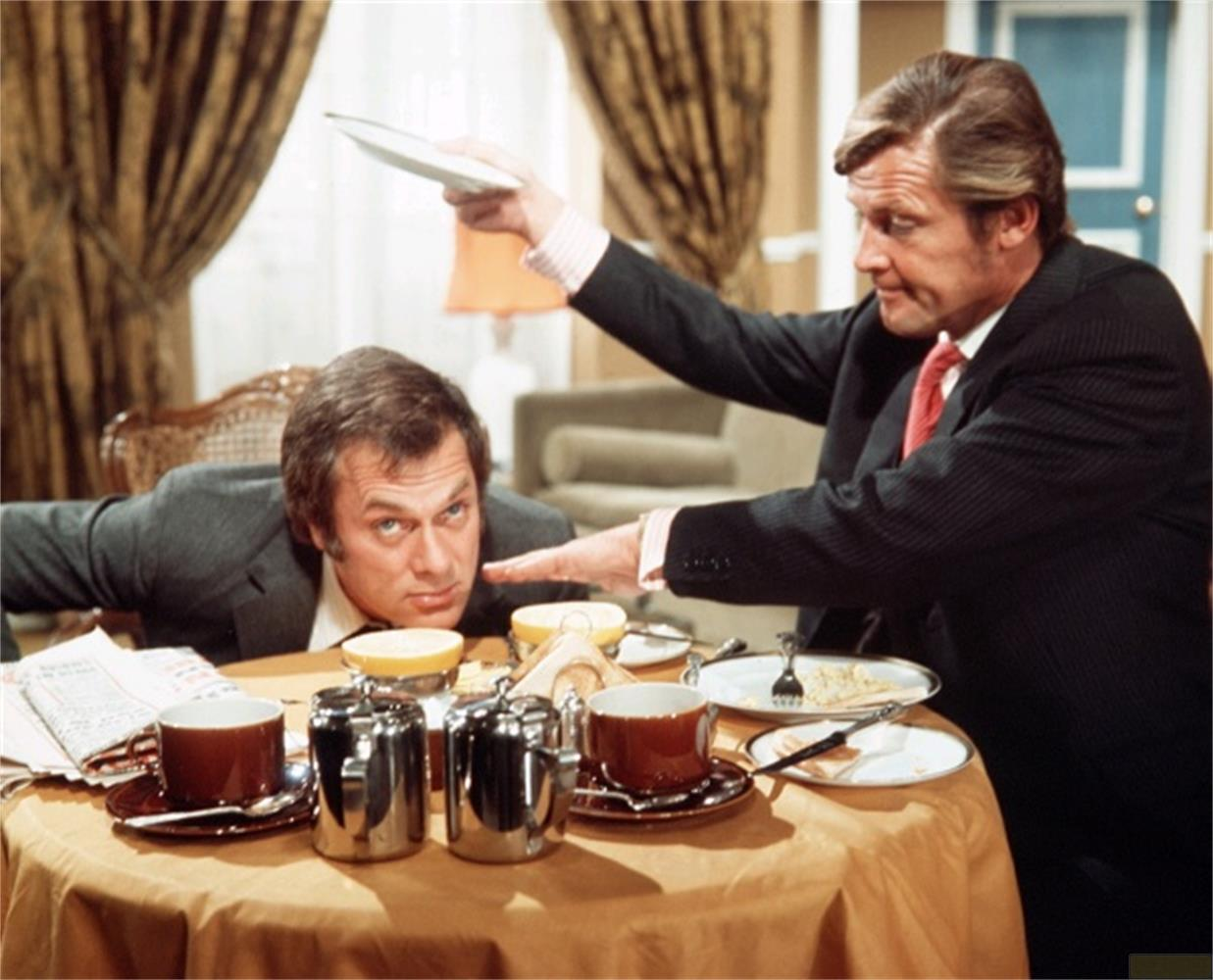 Un homme en costume tient une assiette au-dessus d'un autre homme penché sur une table.