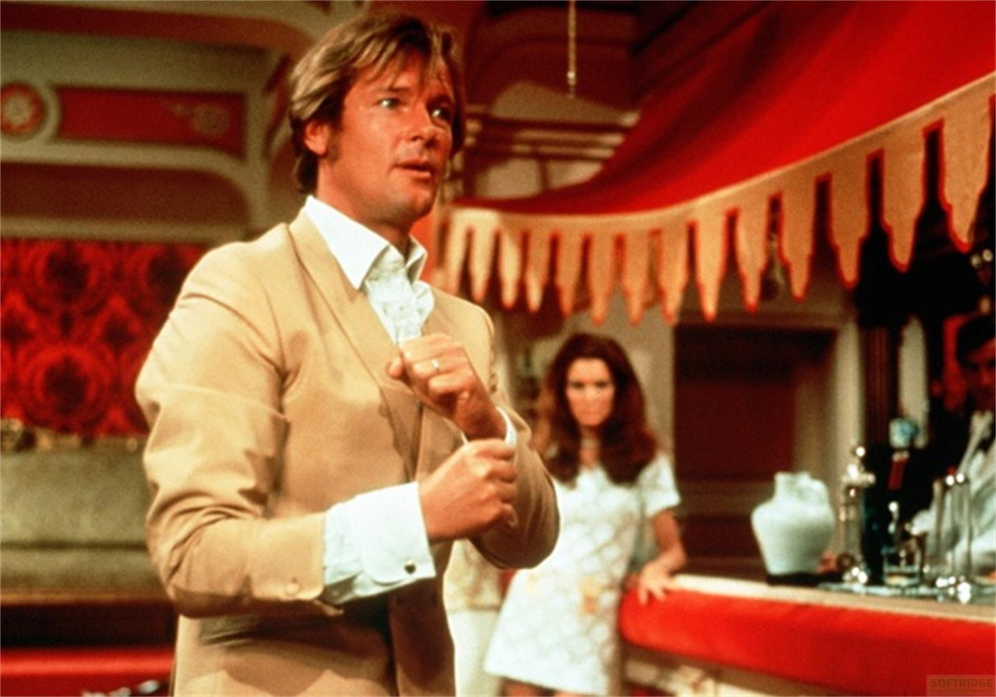 Homme en costume beige, chemise blanche, femme en robe blanche derrière.