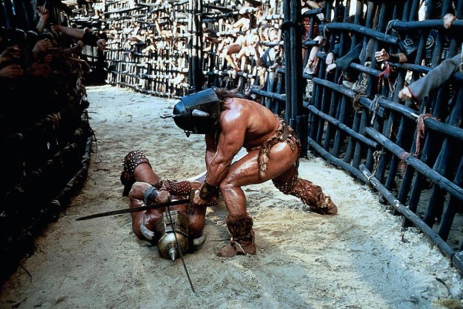 Un uomo in armatura combatte un avversario a terra nella sabbia.