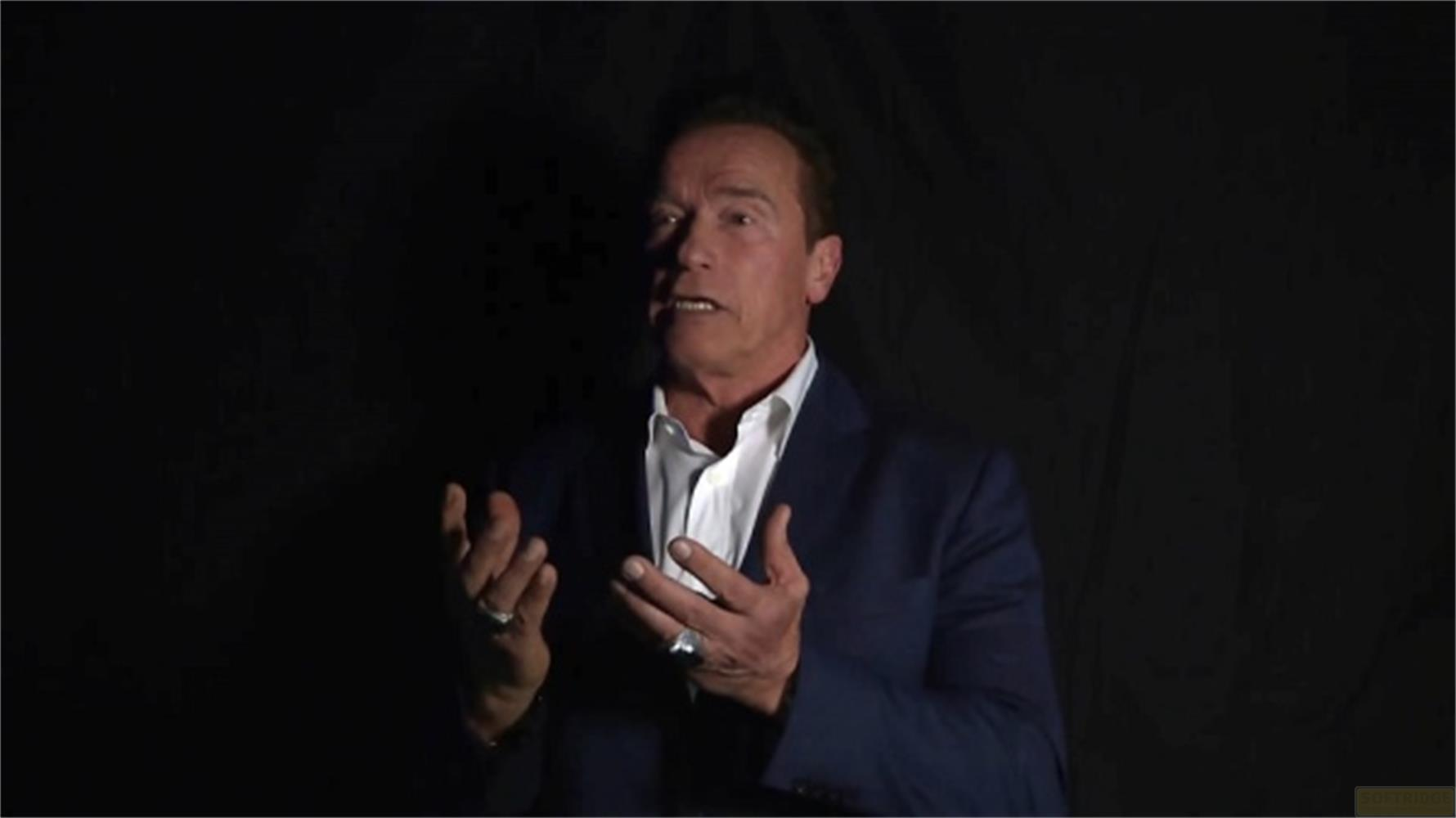 Arnold Schwarzenegger parla con le mani alzate davanti a uno sfondo scuro.