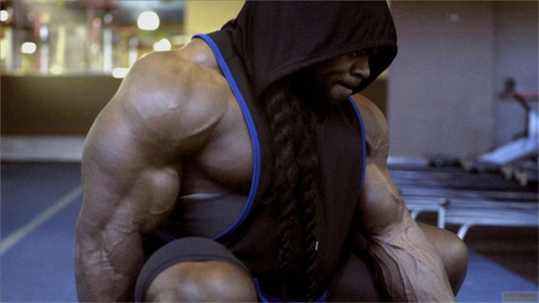 Un bodybuilder con cappuccio e capelli intrecciati si allena in palestra.