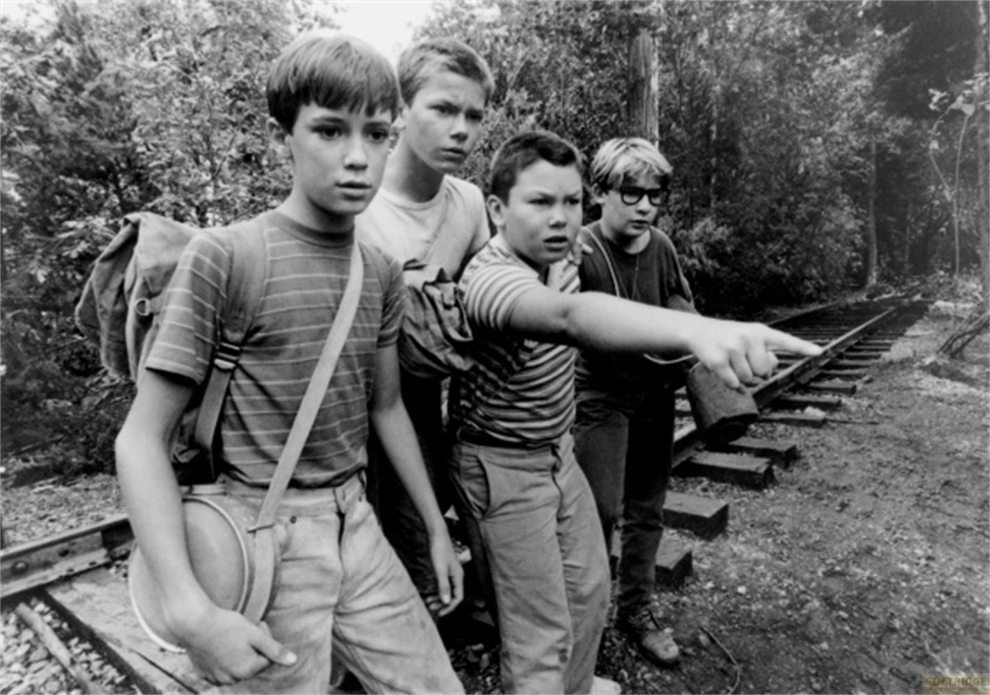 Quattro ragazzi su binari in un bosco, uno punta avanti.