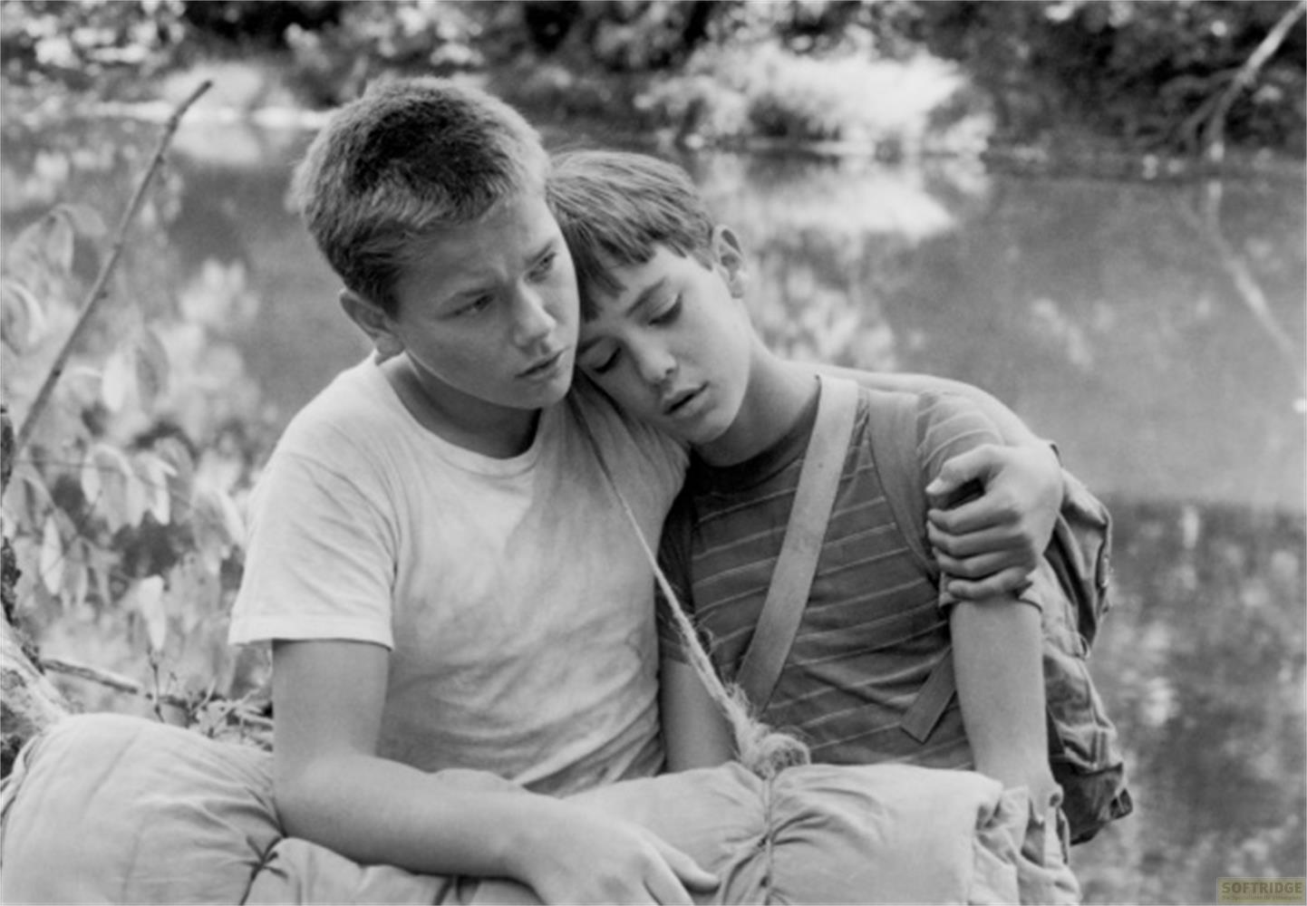 Due ragazzi seduti vicino all'acqua, uno appoggiato all'altro che dorme.