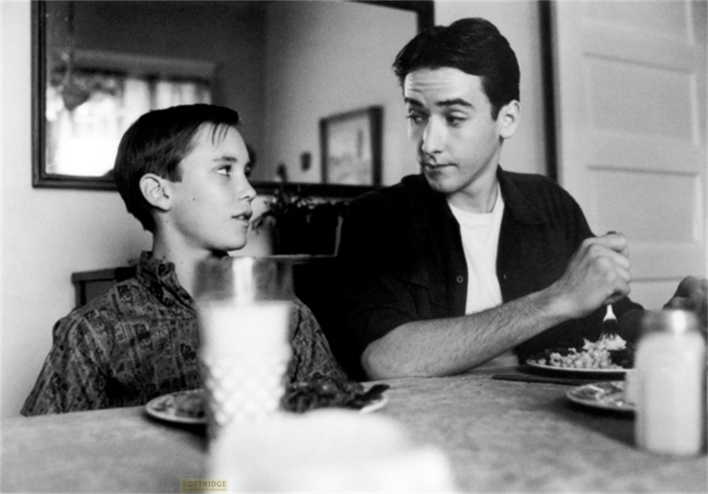 Due ragazzi siedono a tavola a mangiare. Uno parla, l'altro ascolta.
