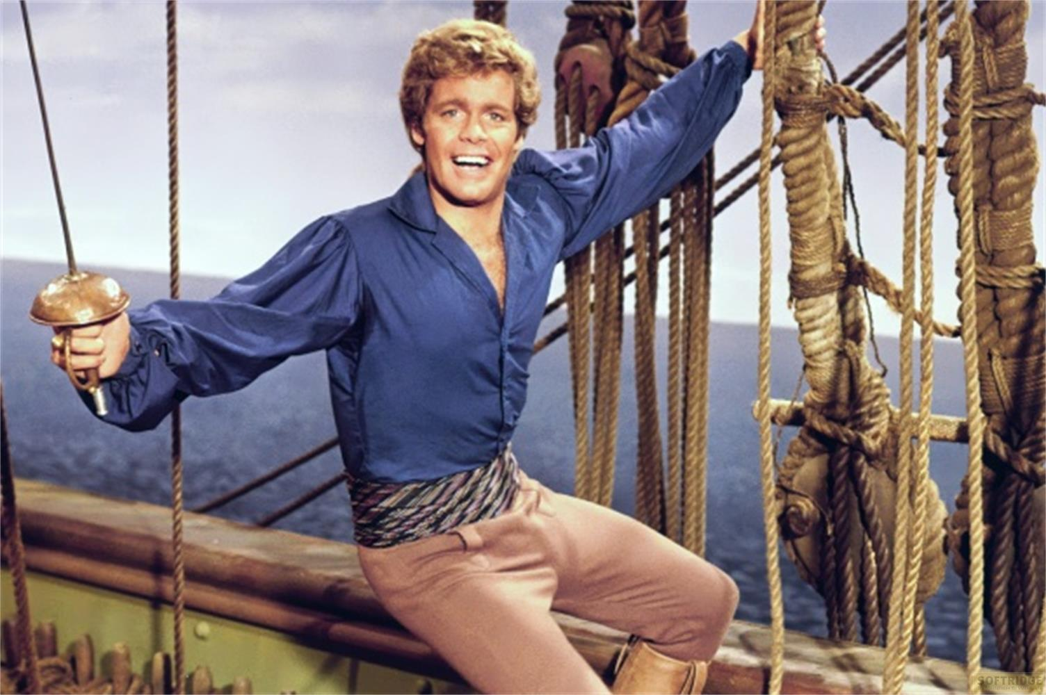 Un uomo in camicia blu e pantaloni marroni tiene una spada su una nave.