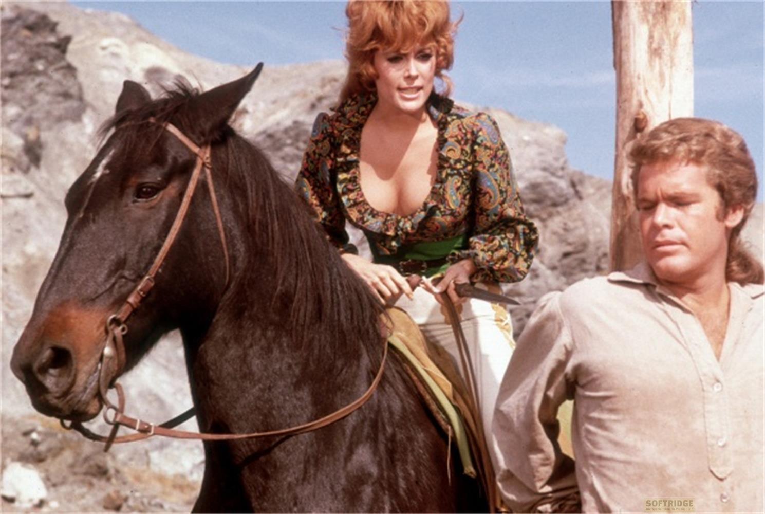 Una donna dai capelli rossi cavalca un cavallo marrone, un uomo le sta accanto.
