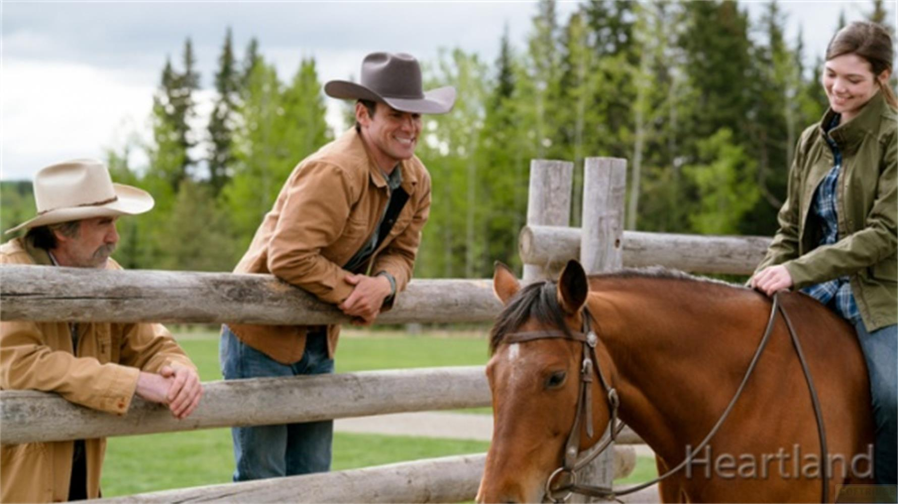 Tre cowboy si appoggiano a una staccionata di legno; una donna cavalca un cavallo marrone.
